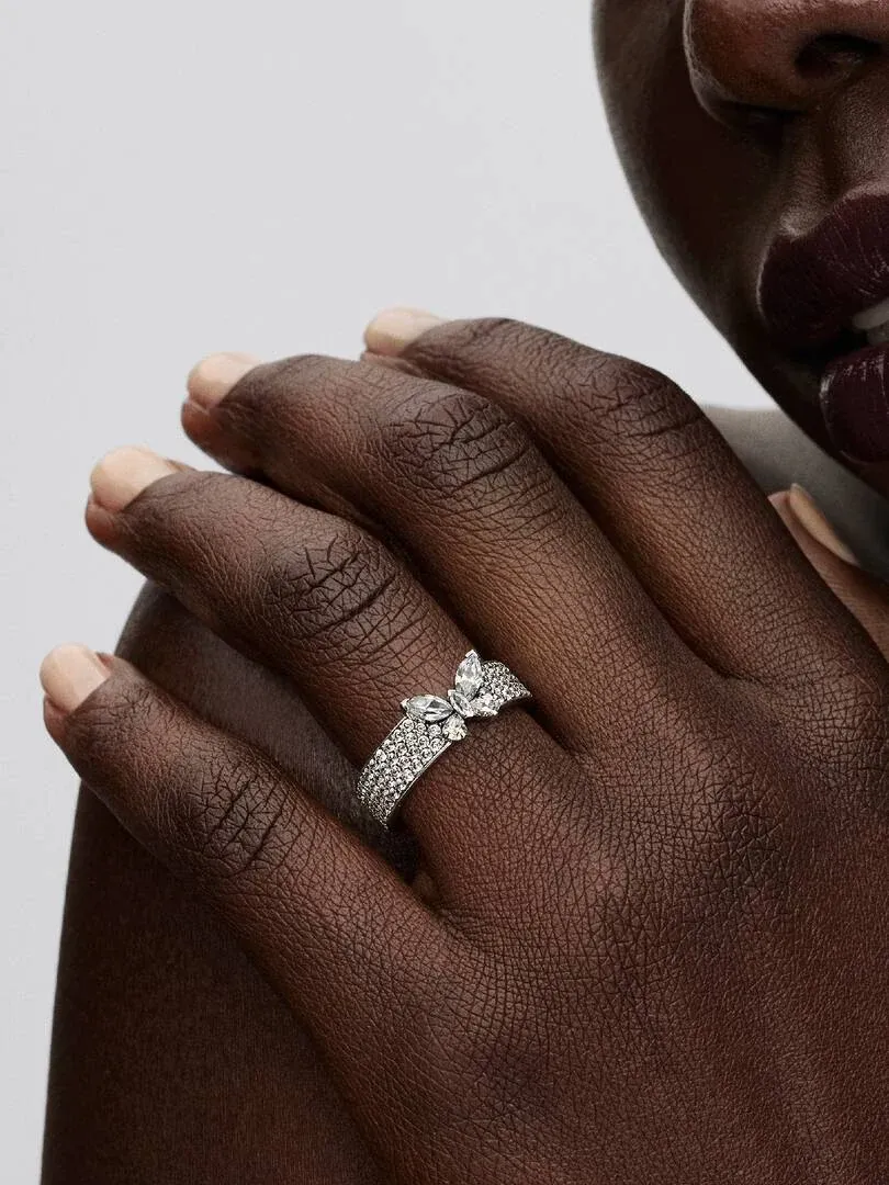 Close-up van de vlinderring om een vinger, zijaanzicht op donkere huid met neutrale achtergrond.