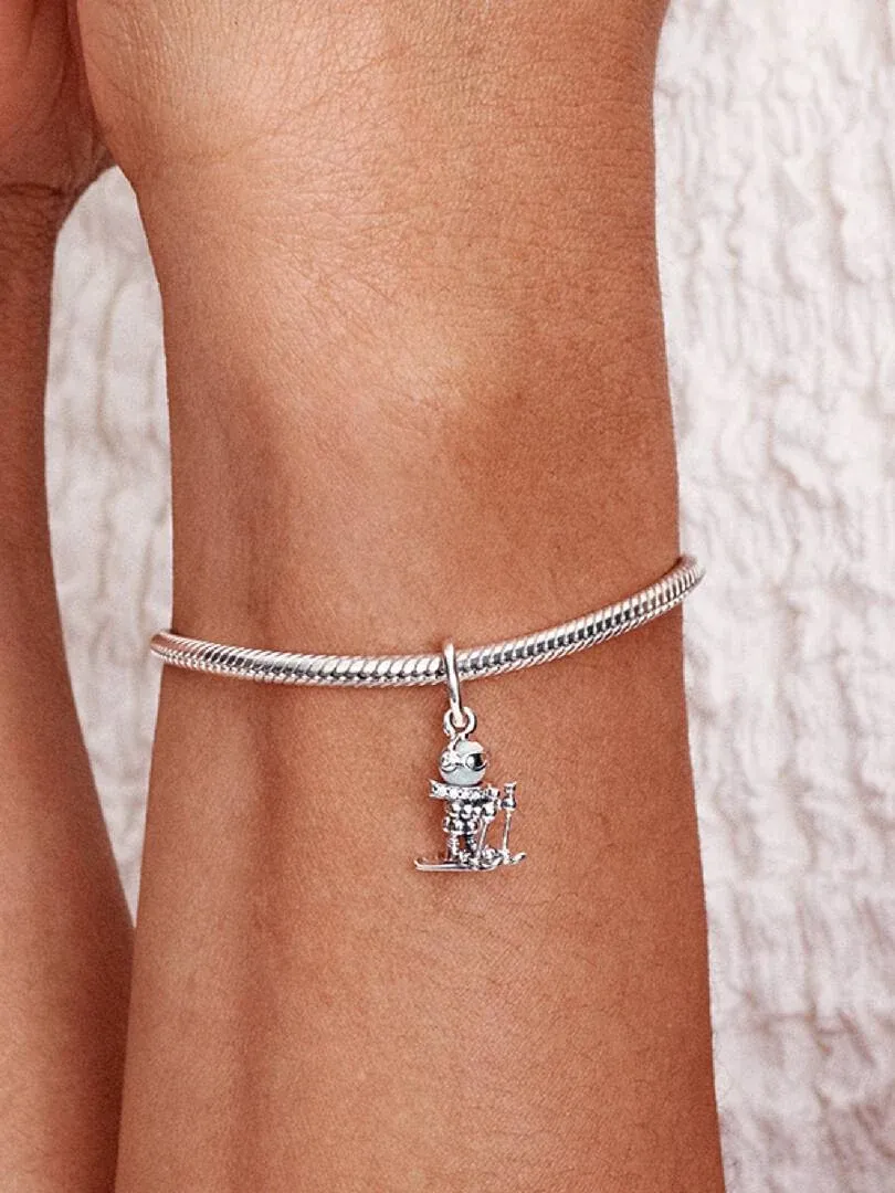 Charm skieur suspendu à un bracelet en argent, vue latérale sur un poignet, fond neutre.
