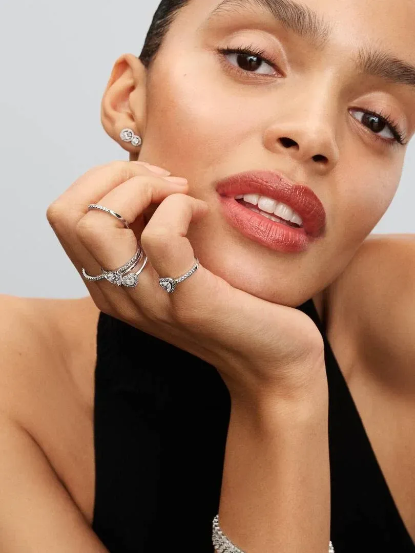 Nahaufnahme einer Frauenhand mit Silberringen, Seitenansicht, die am Kinn ruht vor neutralem Hintergrund.