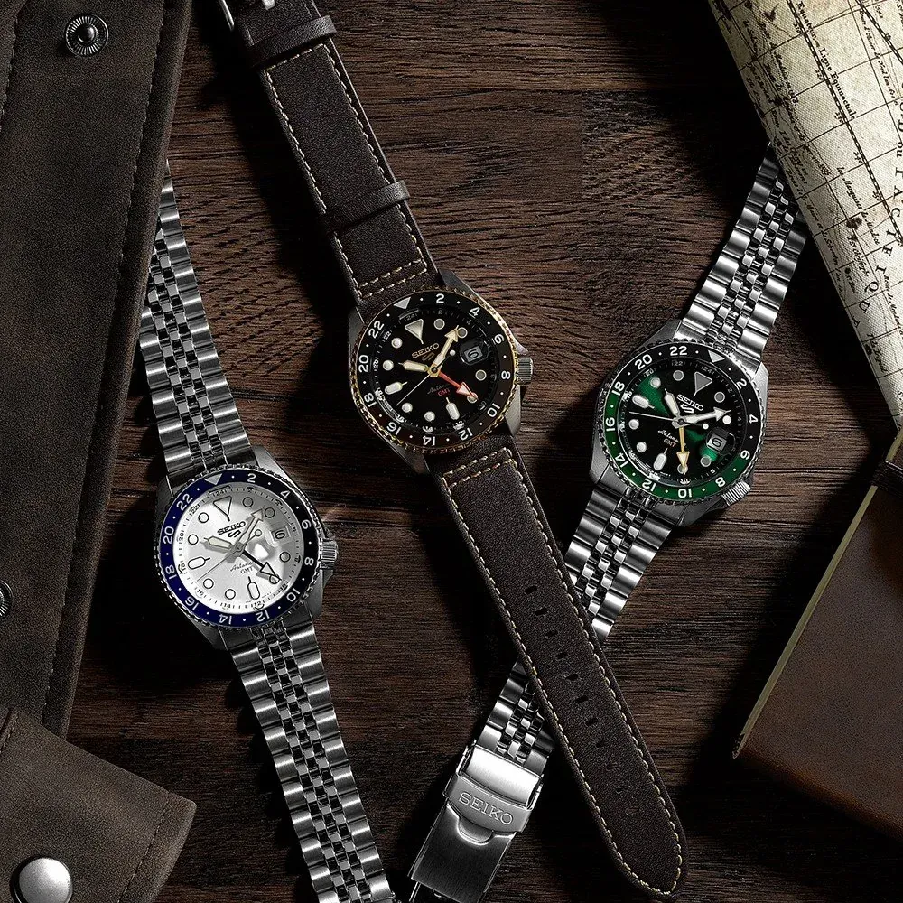 Composición de tres relojes sobre superficie de madera oscura con mapa y accesorios de cuero