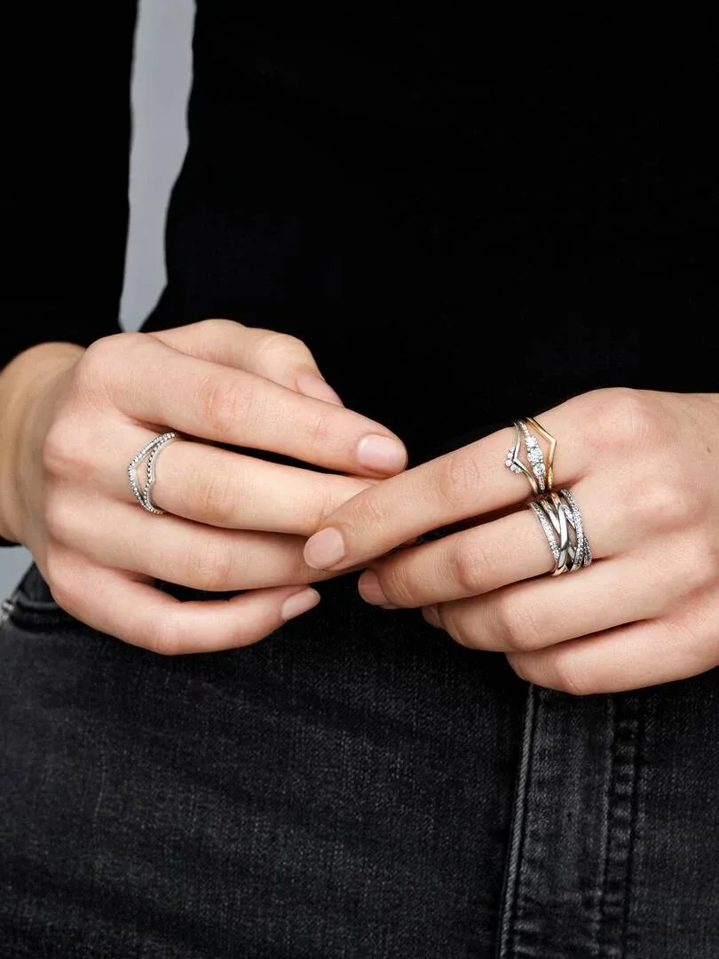 Gros plan de mains portant des bagues en argent et or, vue latérale sur fond sombre et vêtements noirs.