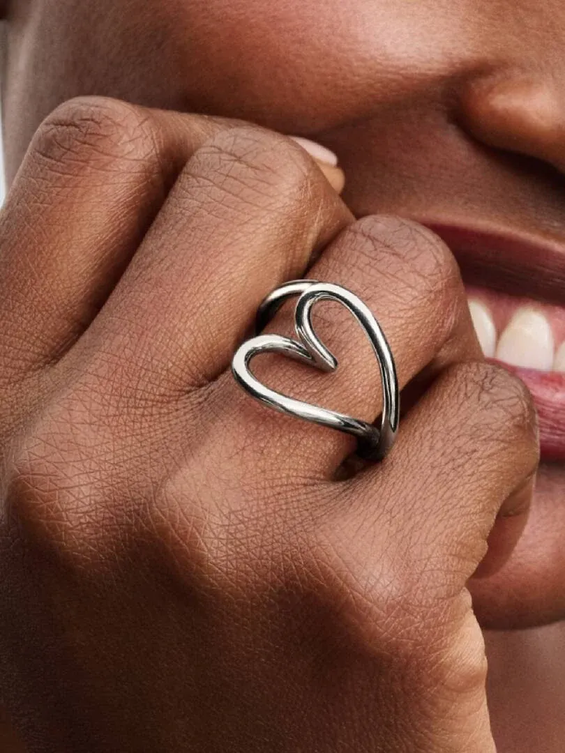 Nahaufnahme des silbernen Herzrings am Finger, Seitenansicht mit unscharfem Gesicht im Hintergrund.