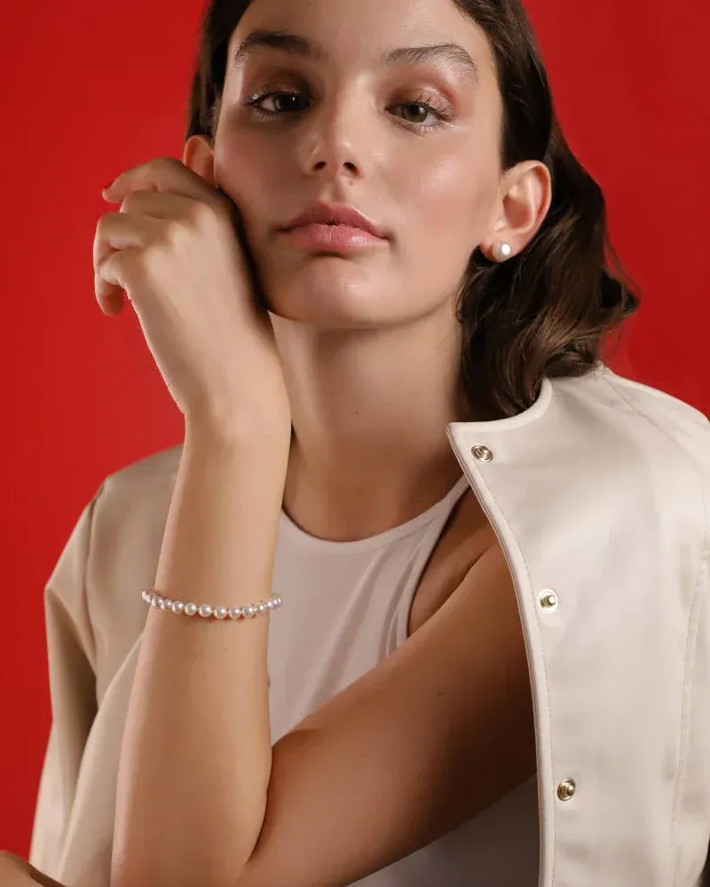 Retrato de modelo luciendo pendientes y pulsera de perlas, fondo rojo vibrante, plano medio.