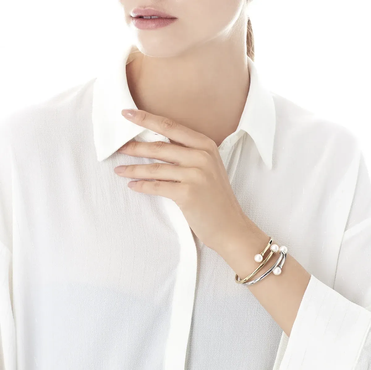 Modelo con camisa blanca y brazalete en la muñeca, pose con mano en el cuello, fondo luminoso.