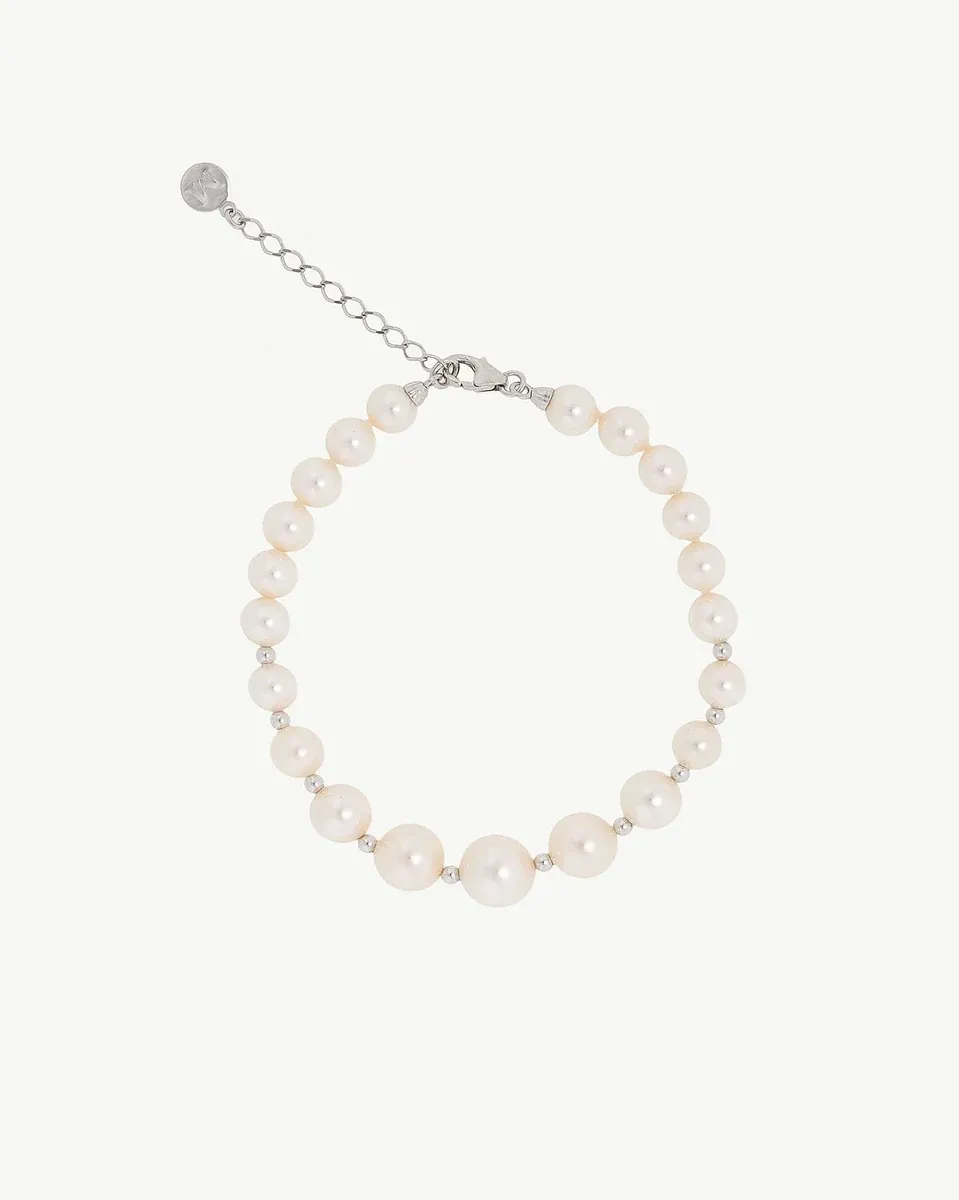 Pulsera de perlas dispuesta en círculo sobre fondo blanco, vista cenital con detalle del cierre y cadena de extensión.