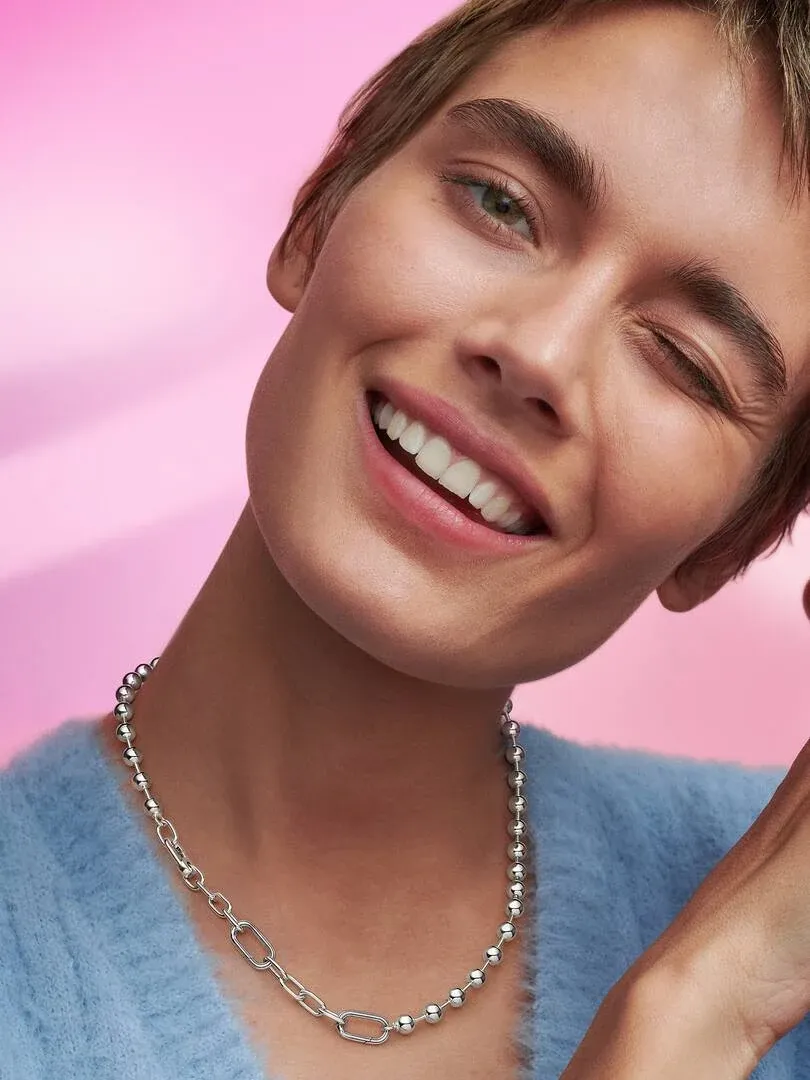 Close-up of a smiling model wearing the link and bead necklace, pink background.