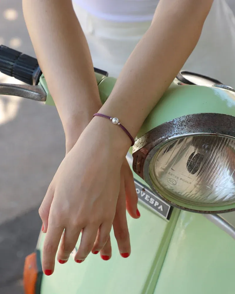 Primer plano de la pulsera con perla en una muñeca apoyada sobre un scooter verde claro, toma lateral.