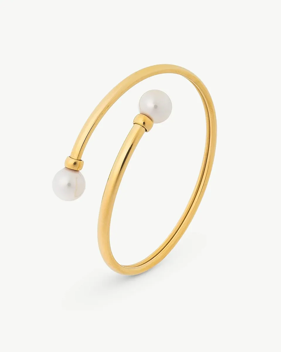 Gouden rigide armband met twee witte parels aan de uiteinden, zijaanzicht op witte achtergrond.