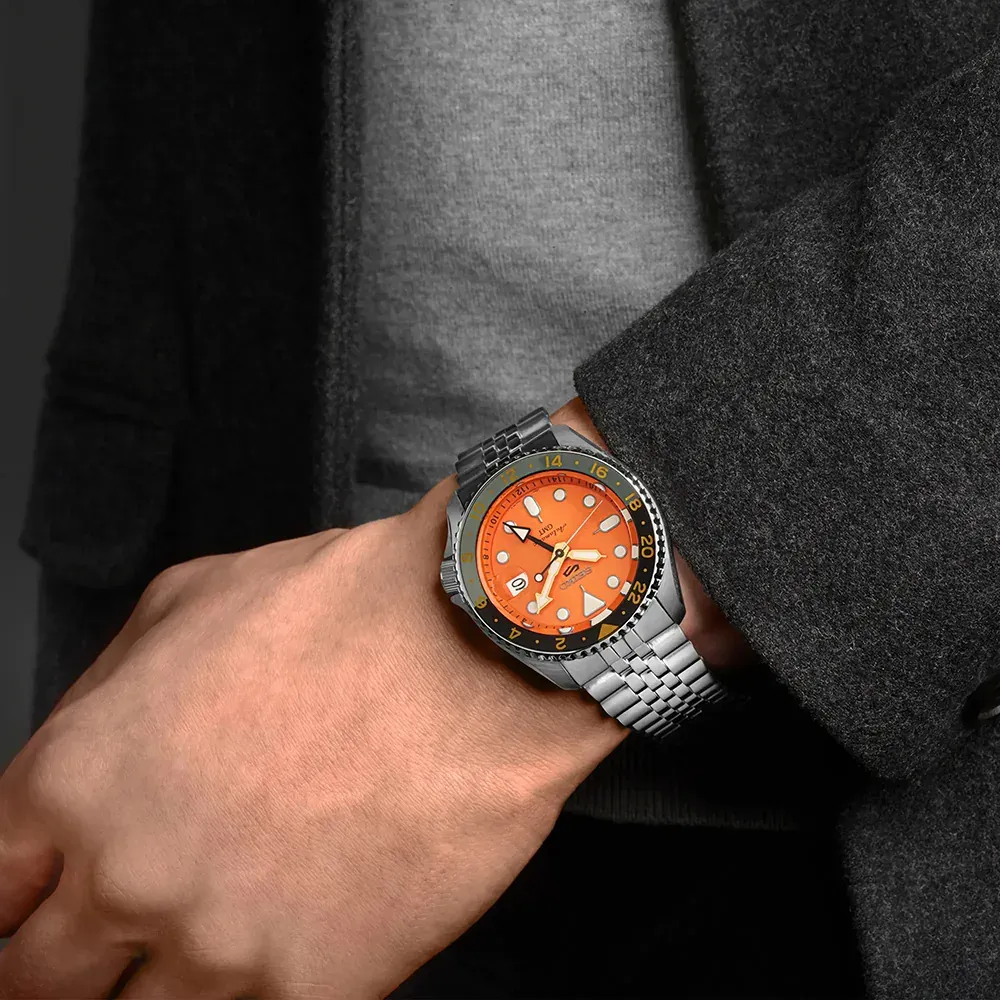 Reloj puesto en muñeca masculina, toma en ángulo, fondo de prendas textiles en tonos grises y negros