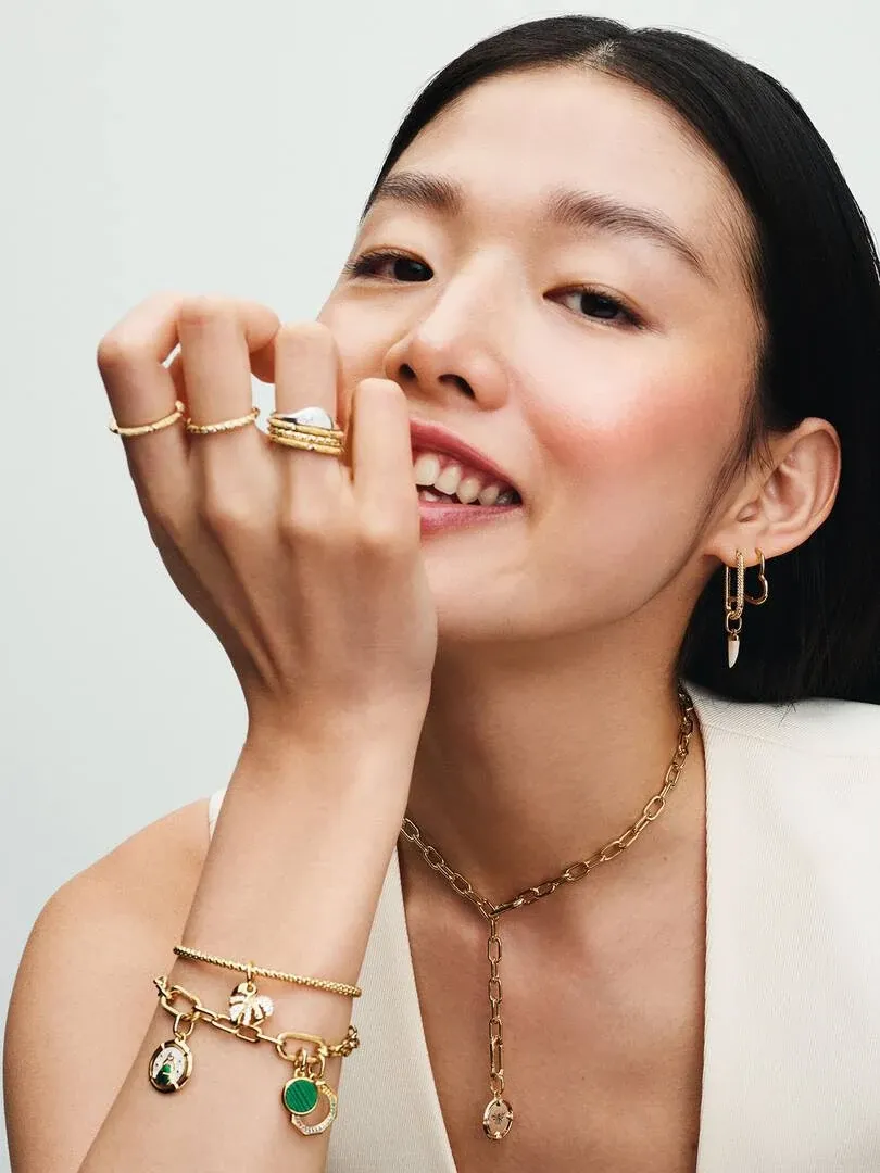 Modelo sonriente con collar de cadena dorada, pendientes de aro y varios anillos y brazaletes de oro.