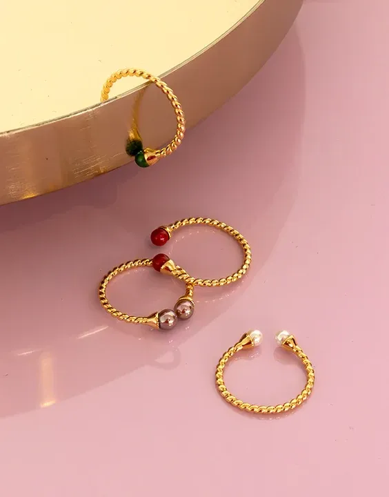 Three twisted design rings with colored pearls on a pink surface and gold base.