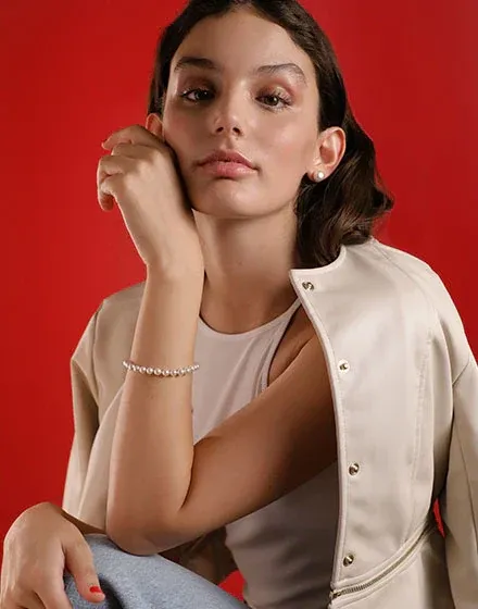 Model wearing pearl bracelet on wrist, medium front shot against vibrant red background.