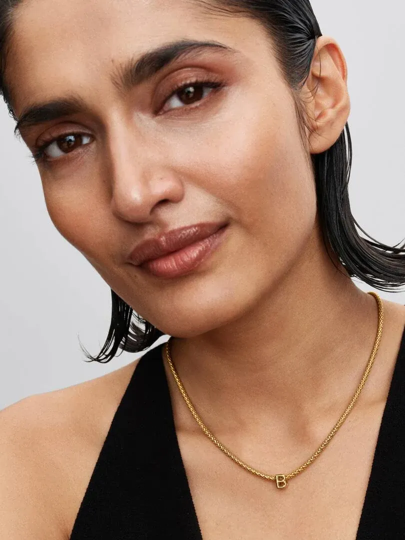 Close-up of letter B charm necklace on model's neck, front view against a neutral background.