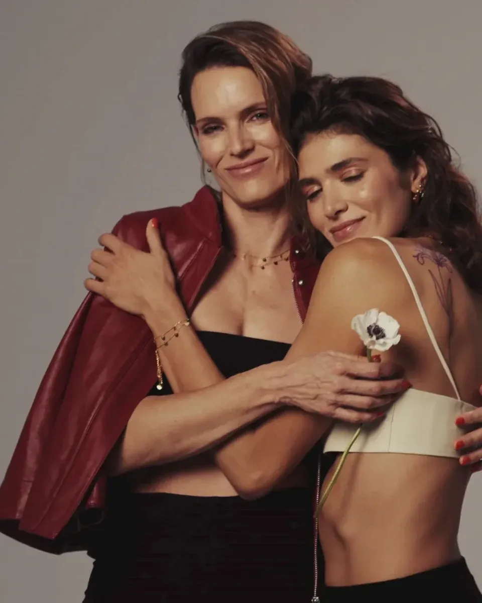 Two models embracing wearing gold jewelry, medium shot, neutral background, focus on necklace and bracelet.