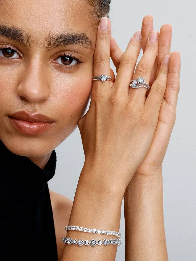 Close-up of hand wearing tennis bracelet and silver rings, side view against a neutral background.
