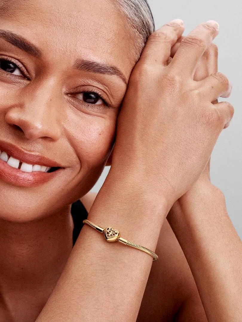Primer plano de la pulsera dorada en la muñeca, toma lateral con modelo sonriente y fondo neutro.