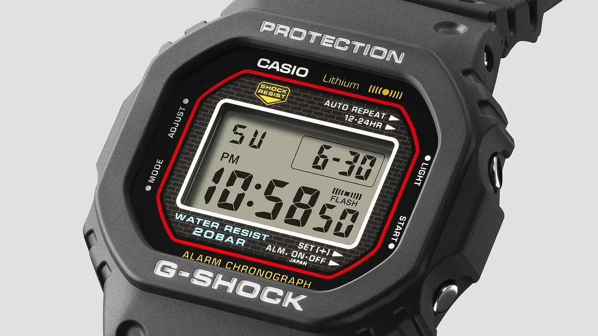 Primer plano en ángulo del bisel y la esfera digital del reloj, fondo gris neutro.