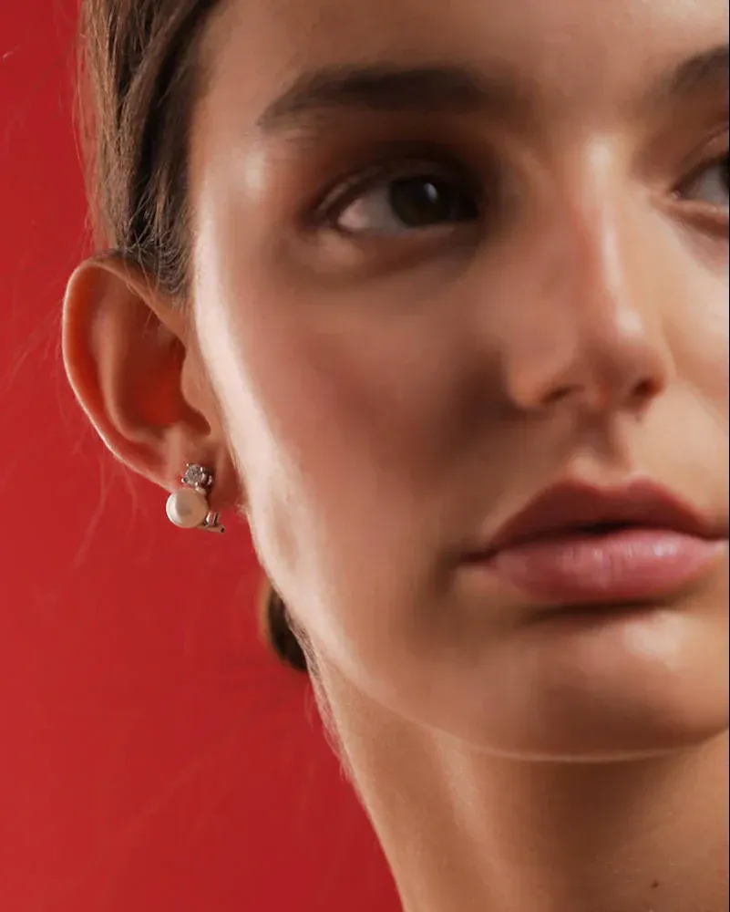 Seitenansicht Nahaufnahme eines Perlen- und Zirkonia-Ohrrings am Ohr, leuchtend roter Hintergrund.