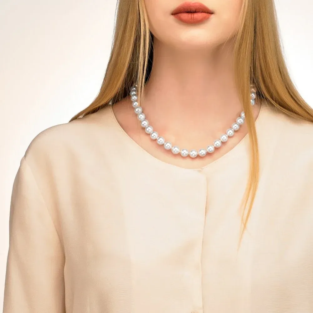 Primer plano del collar de perlas sobre el cuello y escote de una modelo, toma frontal con fondo neutro.