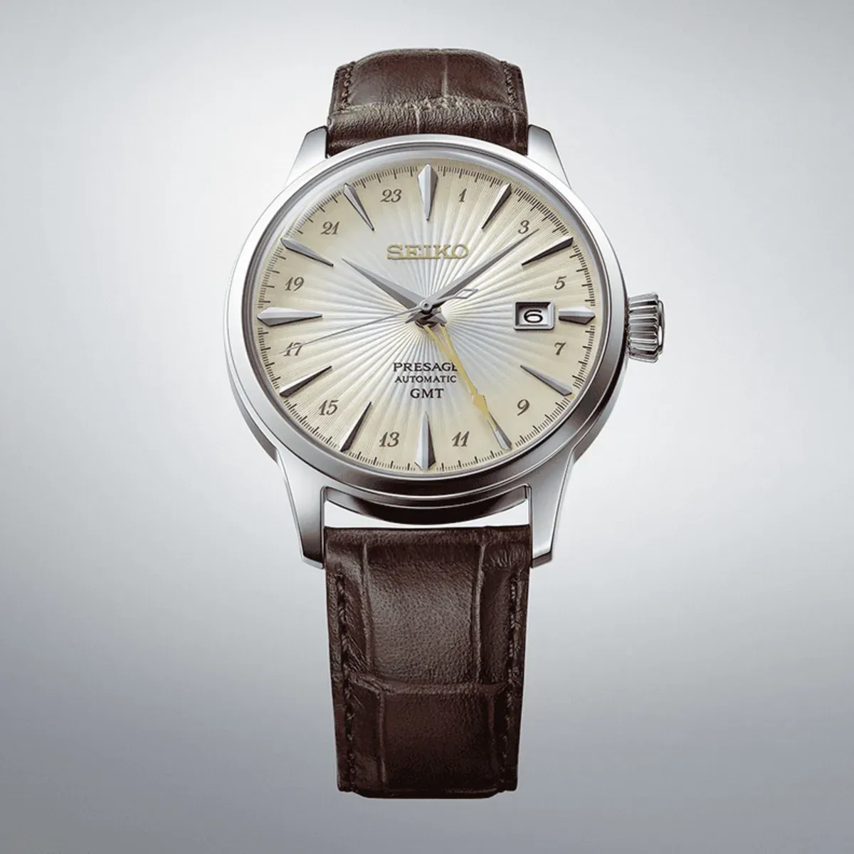 Full front view of the watch on a neutral gradient background, brown leather strap and champagne dial