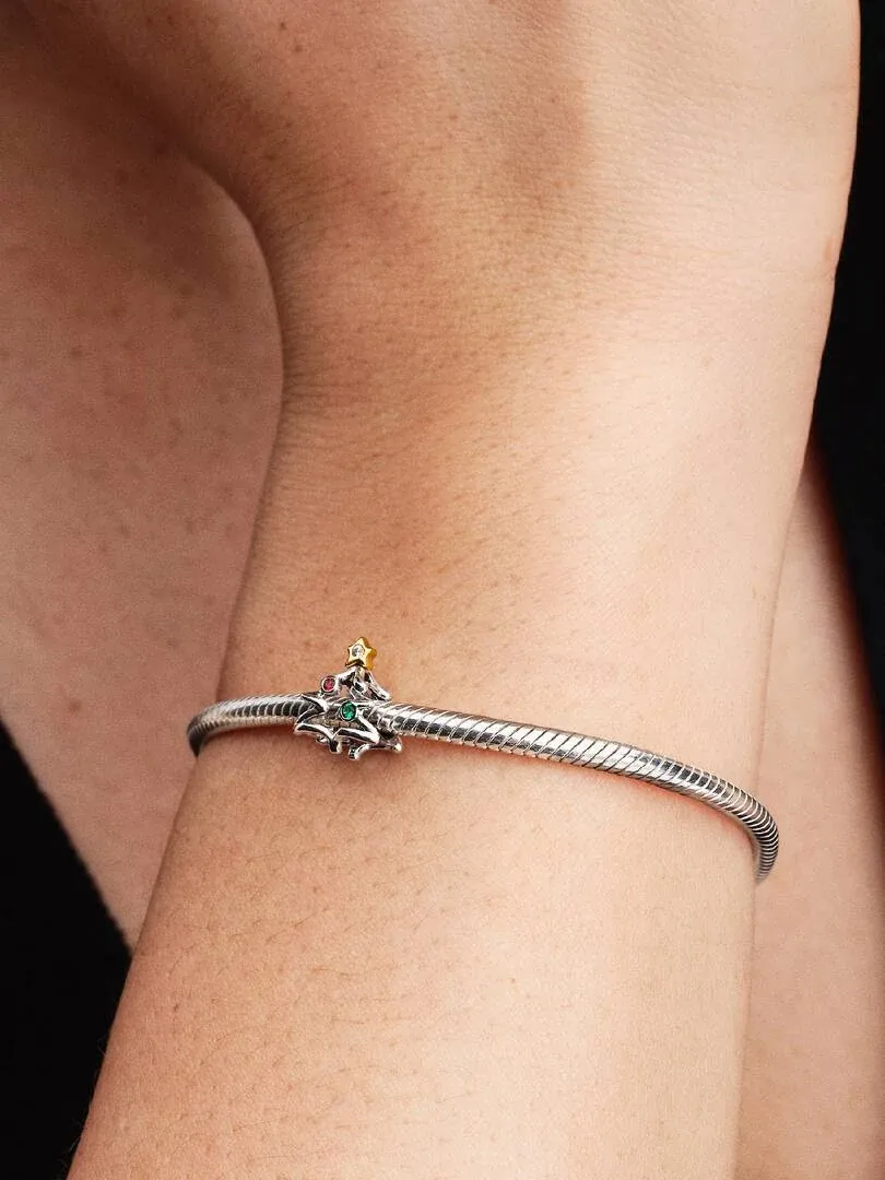 Primer plano de charm navideño con detalles dorados y cristales rojos y verdes en una pulsera, sobre la muñeca.