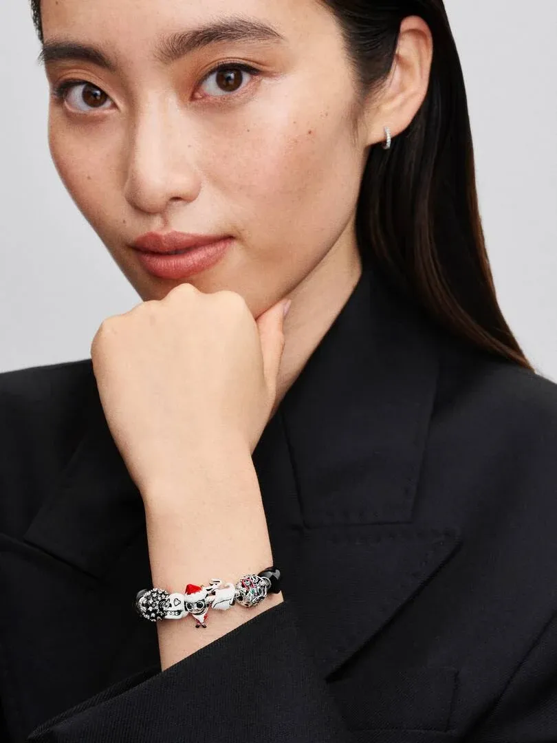 Close-up of a charm bracelet on a model's wrist, side view against a black blazer.