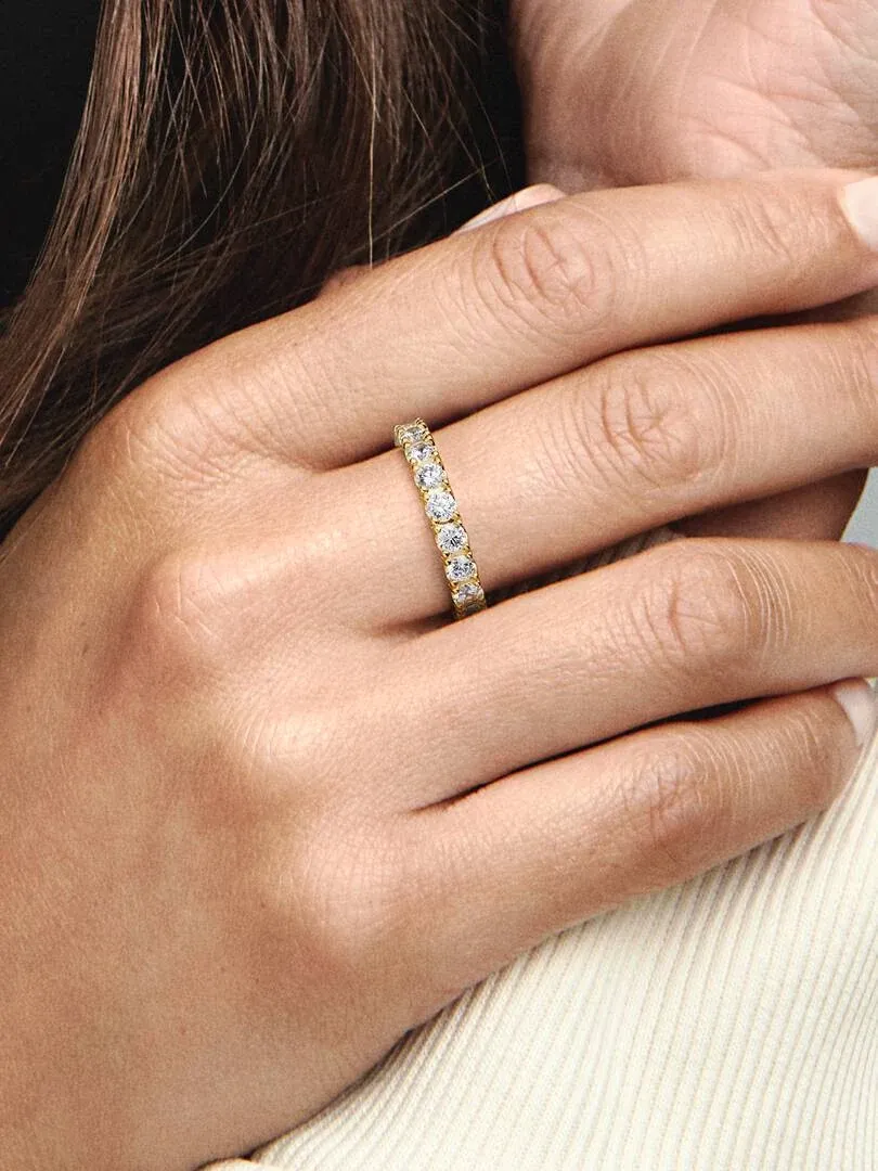 Primer plano lateral de un anillo con circonitas sobre el dedo anular, mano apoyada en la mejilla.