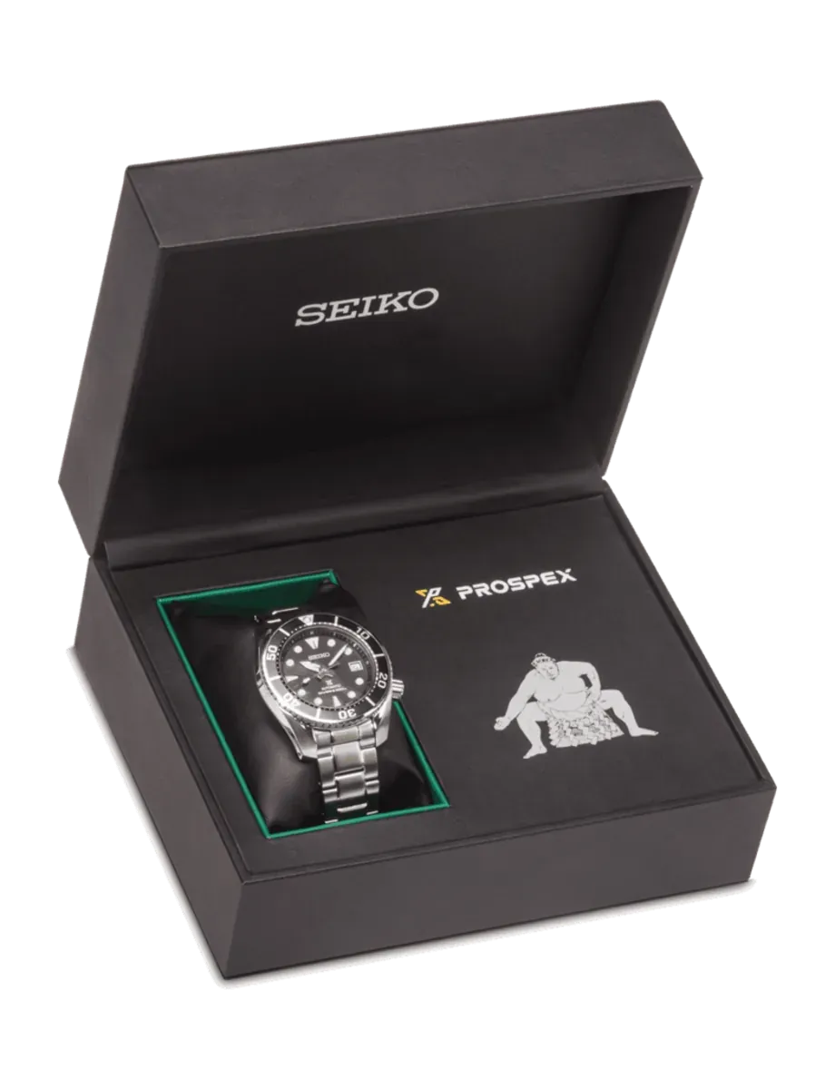 Watch presented in its open black case, angled view, with logos and sumo wrestler graphic.