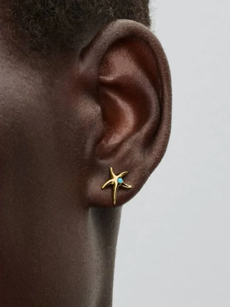 Close-up of gold starfish stud earring with turquoise crystal worn on the earlobe.