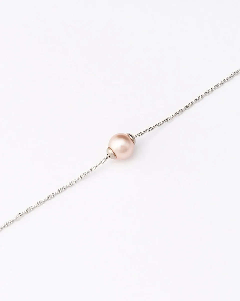 Primer plano de la perla rosa sobre cadena de plata, toma diagonal con fondo blanco neutro.