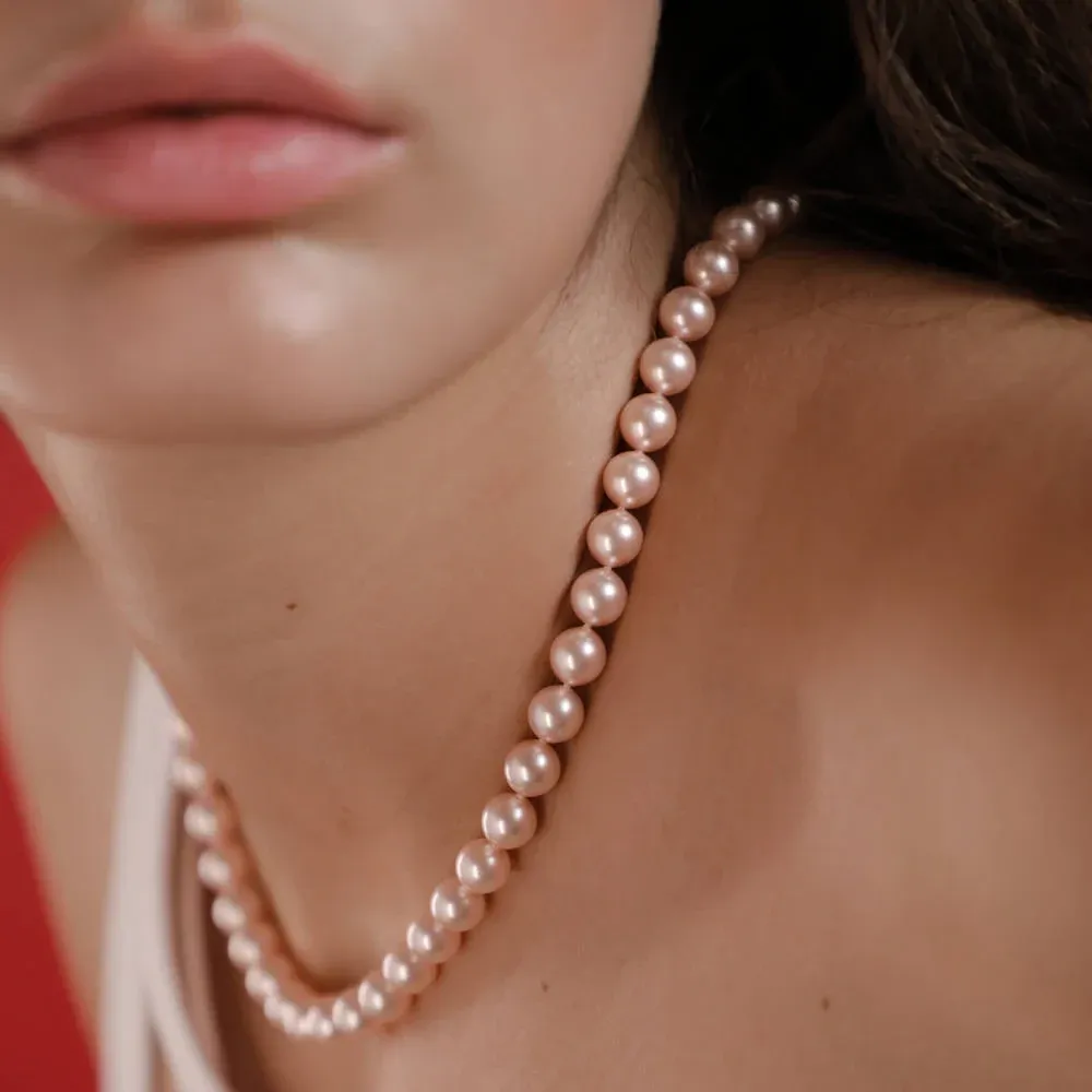 Primer plano del collar de perlas rosas sobre el cuello de una modelo, toma lateral con fondo desenfocado.