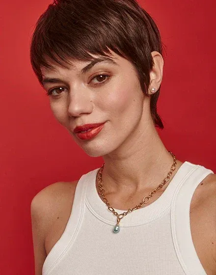 Close-up van model met gouden ketting met turkooise parel, effen rode achtergrond.