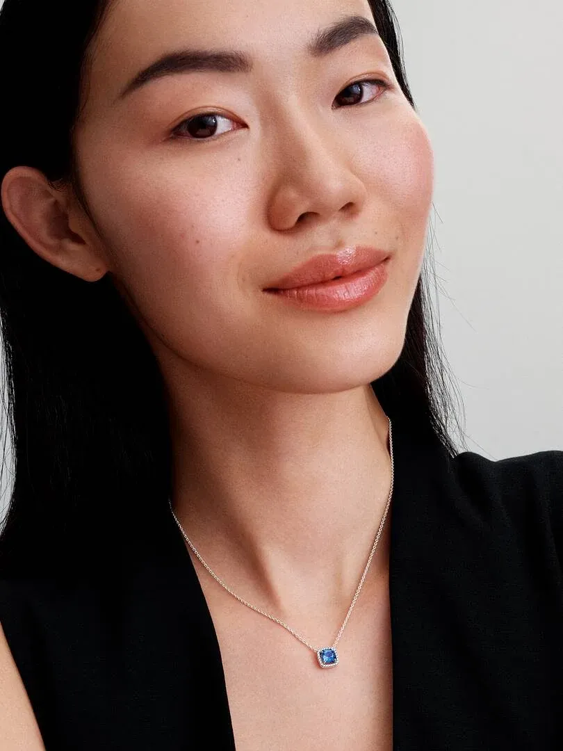 Close-up van de blauwe hanger ketting gedragen om de hals van een model, lichte neutrale achtergrond.