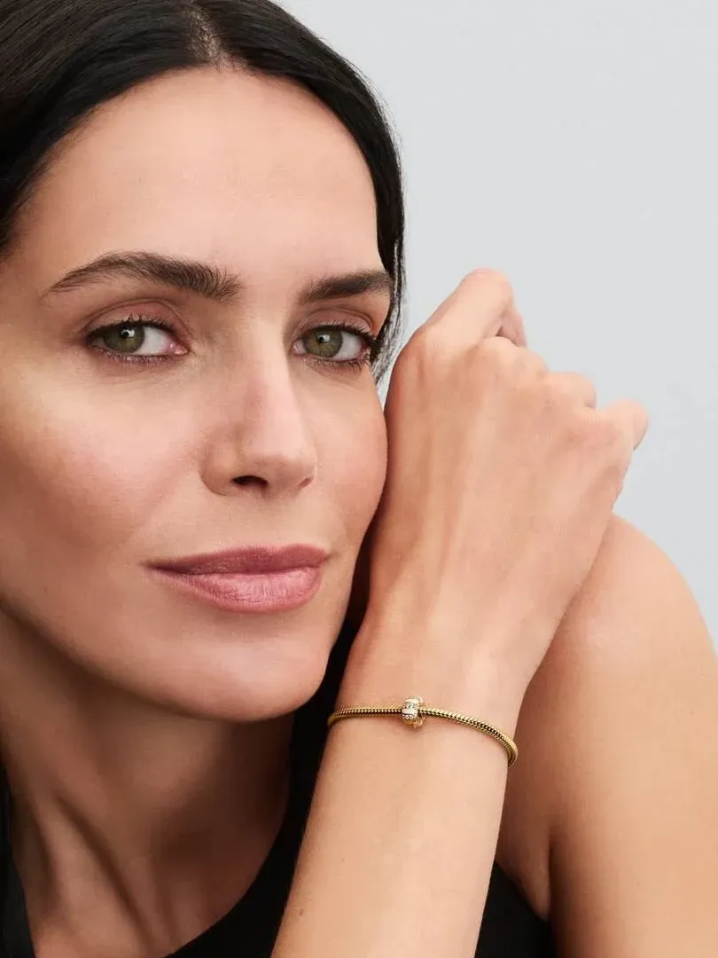 Nahaufnahme des Handgelenks mit dem goldenen Clip-Charm, Seitenansicht an einem Model vor neutralem Hintergrund.