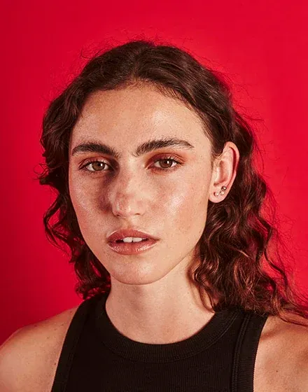 Close-up side view of an ear wearing a pearl stud, model against a vibrant red background.