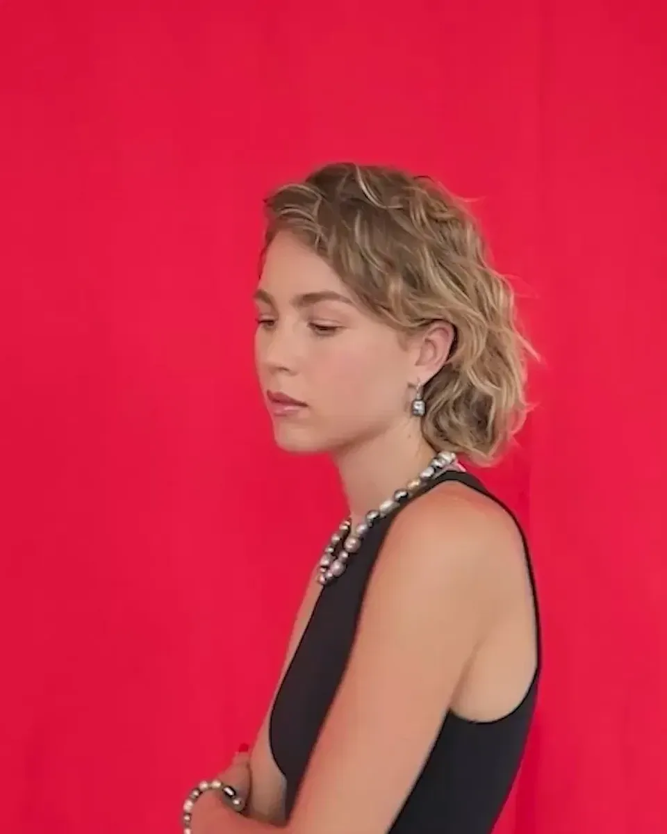 Model van opzij met parelketting en parelarmband tegen een dieprode achtergrond, medium shot.