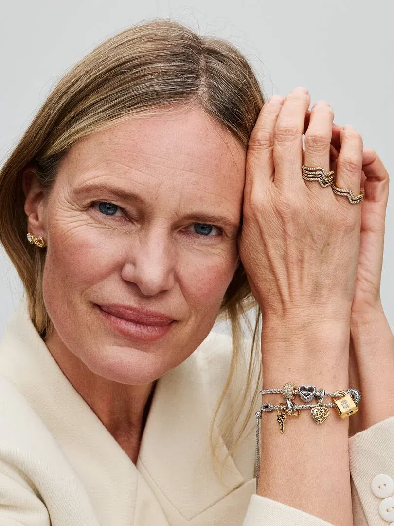 Close-up van een vrouw met een charmeparelband en gouden ringen, zijaanzicht leunend op haar gezicht.