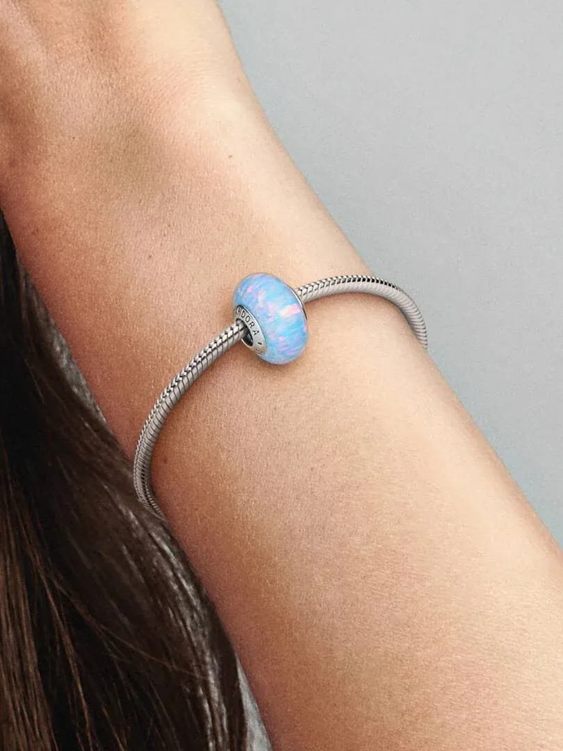 Gros plan du charm bleu sur un bracelet en argent porté au poignet, vue de profil avec fond flou.