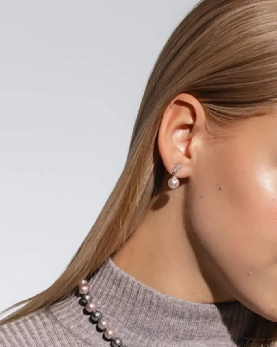 Gros plan latéral d'une boucle d'oreille en perle blanche portée à l'oreille, fond neutre clair.