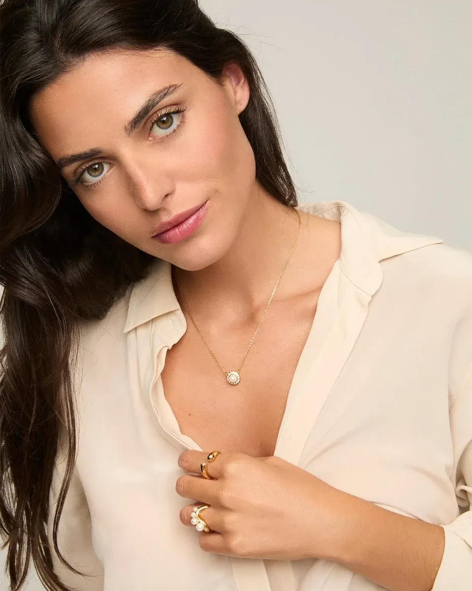 Primer plano del collar con colgante de perla sobre el cuello de una modelo, toma frontal con camisa clara.