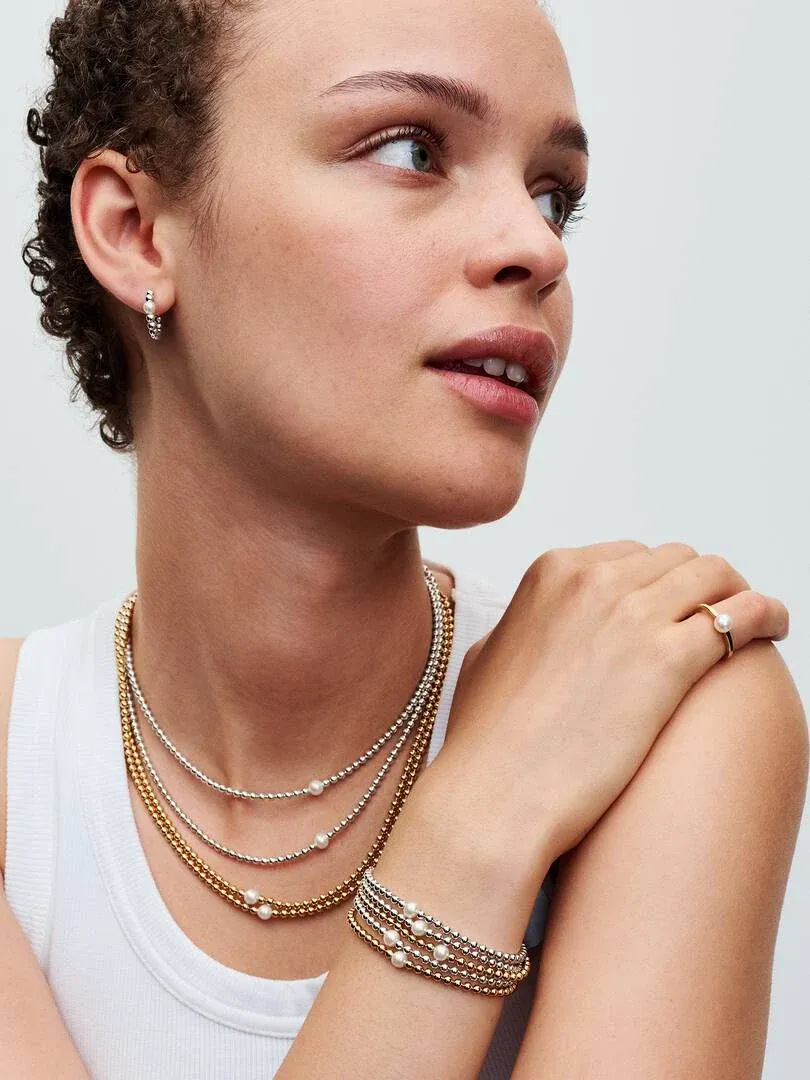 Model trägt Perlen- und Kugelhalsketten, passendes Armband und Ring vor weißem Hintergrund.