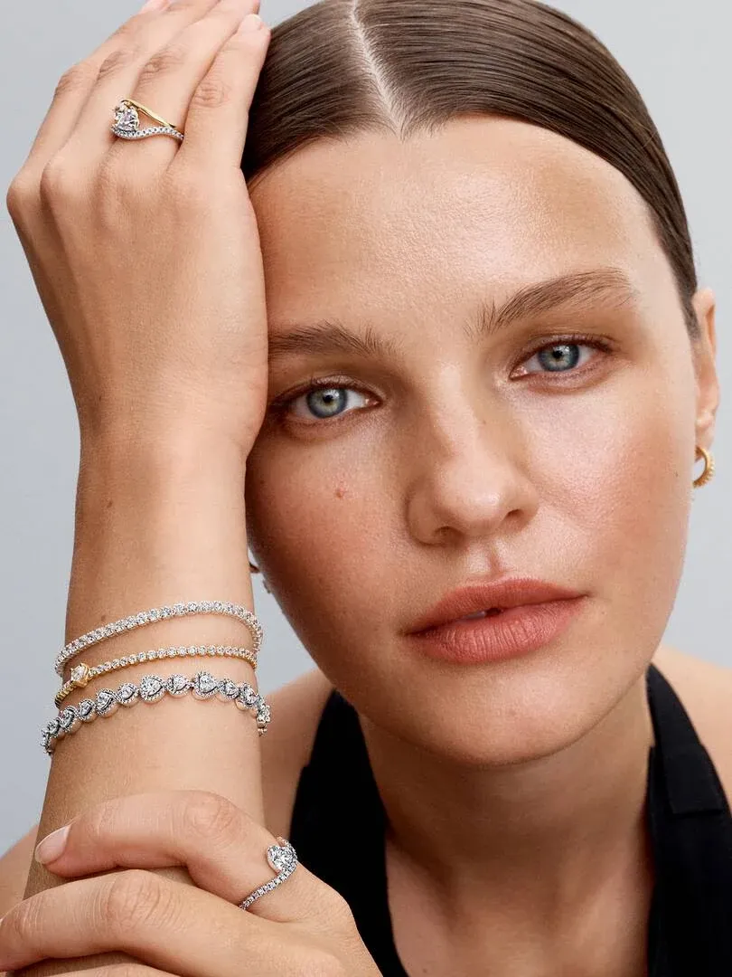 Gros plan d'un modèle portant des bagues et un bracelet doré, vue de profil sur la main et le visage.