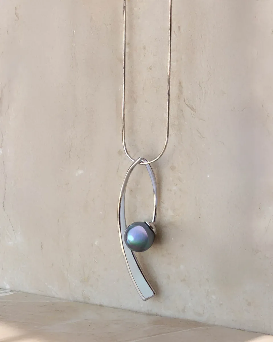 Collar con colgante de perla gris sobre fondo de piedra neutra, toma frontal con iluminación suave.