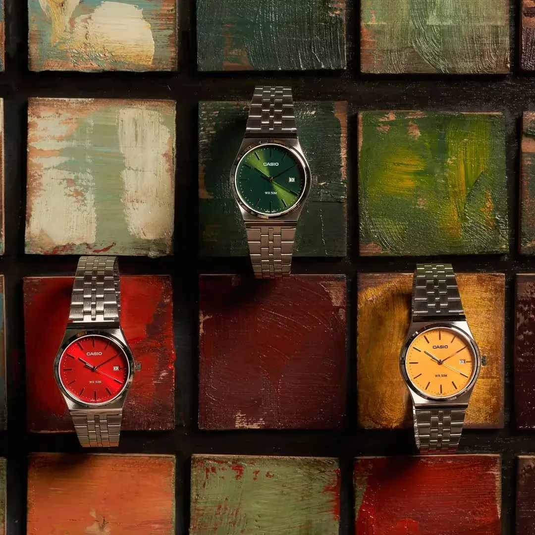 Vista cenital de tres relojes con esferas verde, roja y amarilla sobre un fondo de bloques de colores pintados.