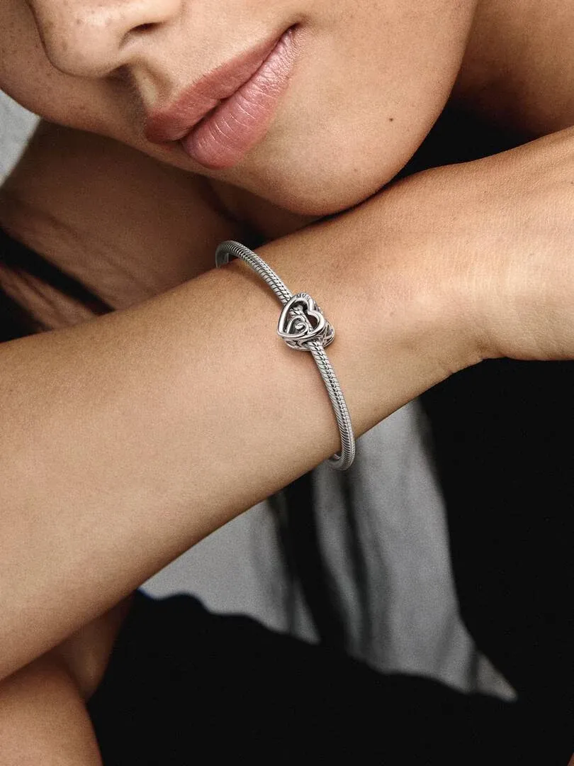 Close-up van de verstrengde harten charm aan een armband, gedragen om de pols van een model.