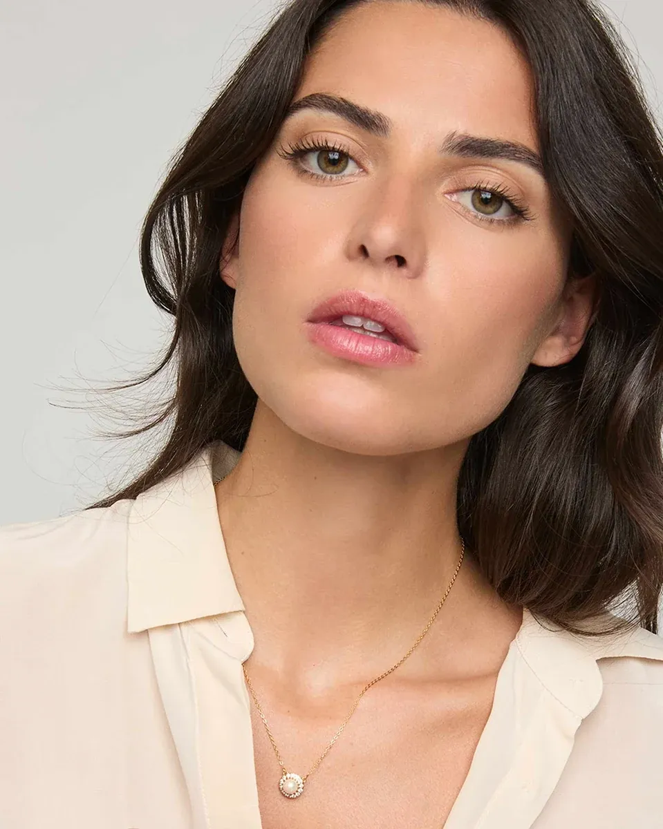Primer plano del collar con colgante de perla sobre el cuello de una modelo, fondo neutro claro.