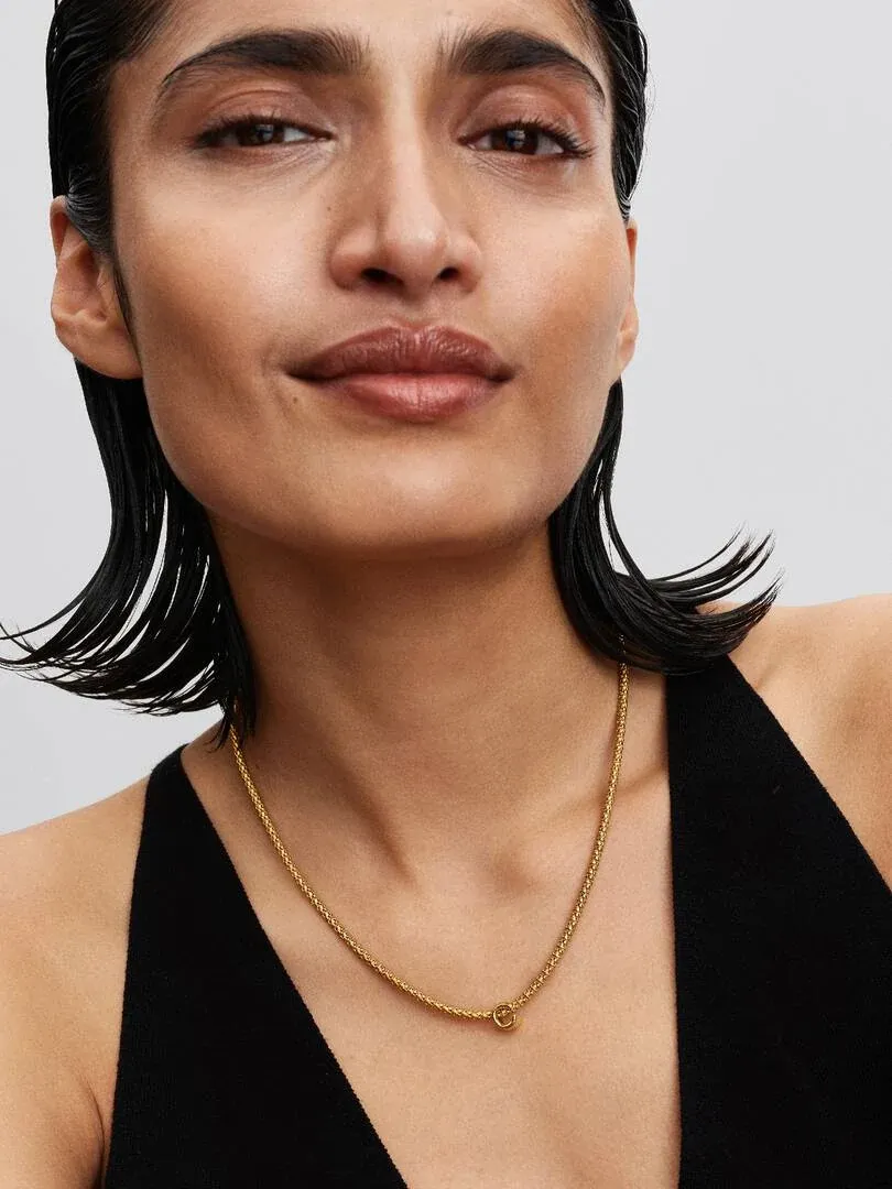 Nahaufnahme einer goldenen Halskette mit Buchstaben-C-Charm an einem Model, Frontansicht auf Halshöhe.