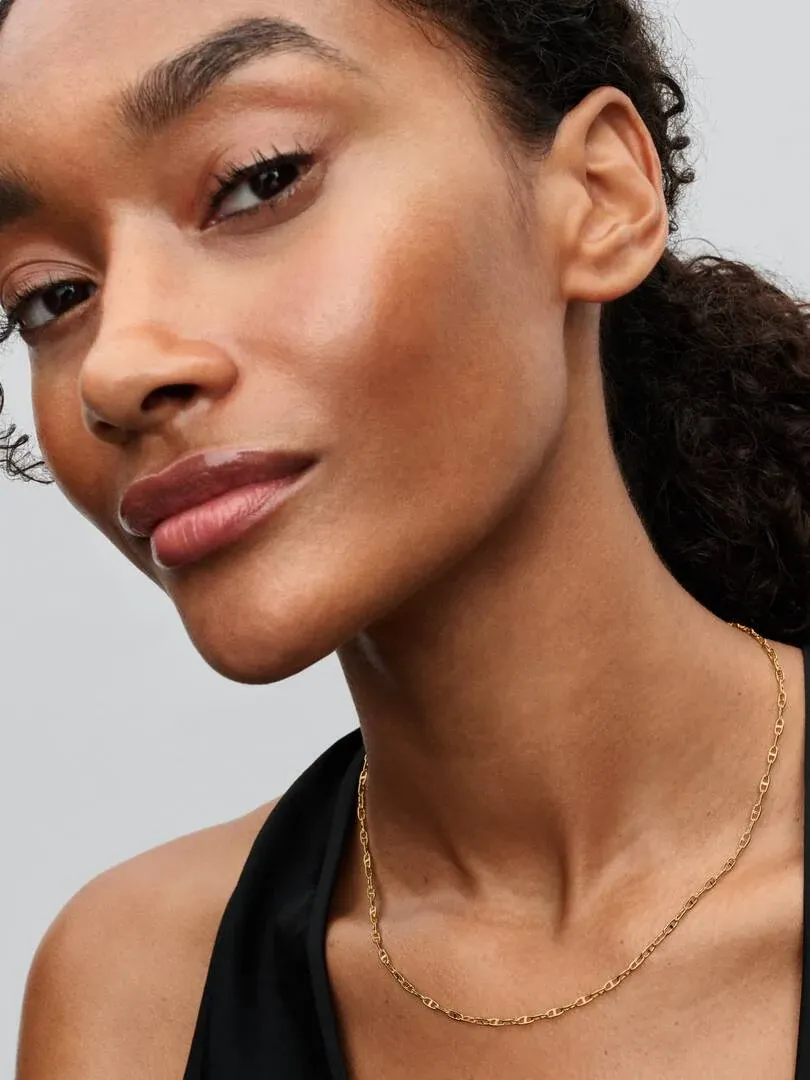 Close-up of the gold chain necklace on a model's neck, side view against a neutral background.