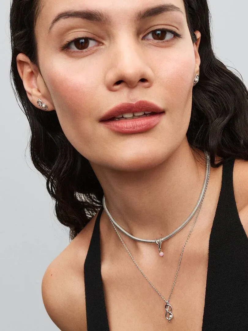 Close-up of a model wearing knot hoop earrings and a chain necklace, front view against a grey background.