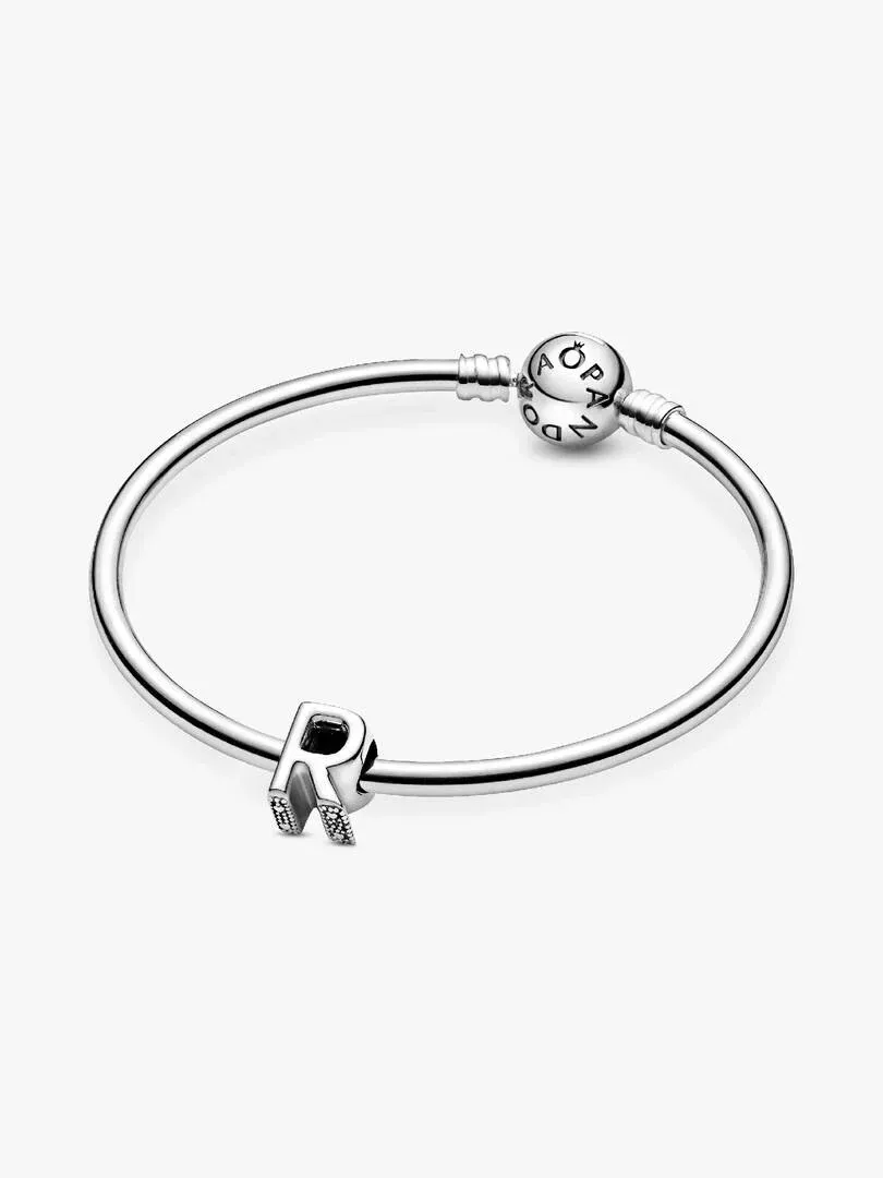Charm de letra R en plata sobre una pulsera rígida, vista frontal con ángulo ligeramente picado y fondo blanco.